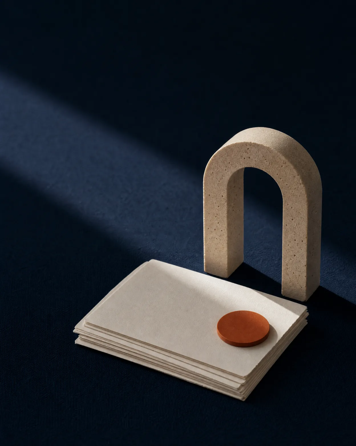 Arche en pierre, cartes ivoire et sceau orange sur un textile bleu nuit